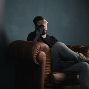 A man holds his head in distress while sitting on a couch