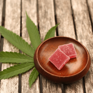 a brown wooden plate holding two red cannabis gummies