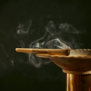 a joint with white smoke burning over an elevated ashtray 