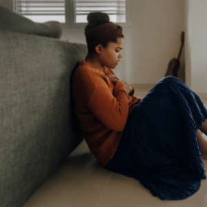 a woman sitting against a couch with her hands on her chest in an anxious position