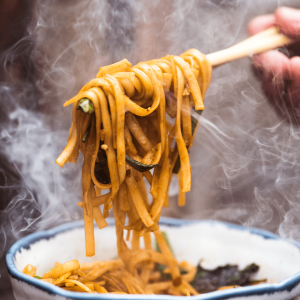 A person holding chopsticks and scooping up noodles