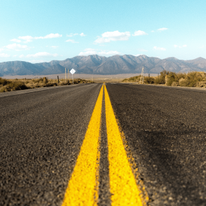 a gray asphalt road leading to California hills in the distance