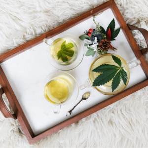 Wooden tray pictured with cannabis drinks and leaves on top