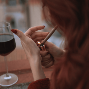 a girl lighting a joint and drinking a glass of red wine