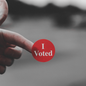 person holding a red ‘i voted’ sticker