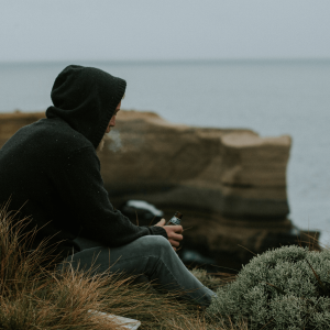 a man sitting on a cliff smoking and drinking 