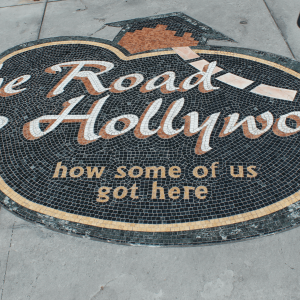 a black and brown street sign saying ‘the road to Hollywood’