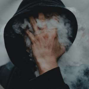 a person in a black hoodie blowing out smoke