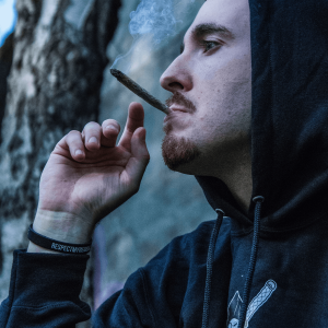 a man in a black hoodie smoking a joint