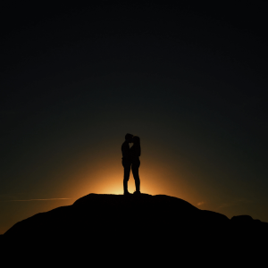 a silhouette of a man and woman kissing on top of a mountain