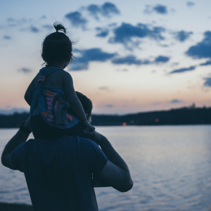 a dad with a daughter on his shoulder overlooking a lake
