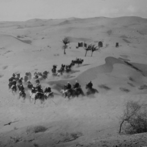grayscale photo of horses riding through sand dunes