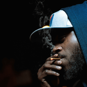 a man with a hat and blue hoodie smoking a blunt