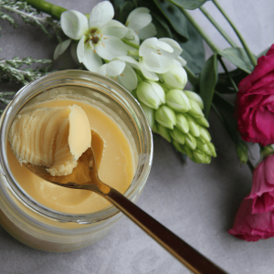 a jar of butter with spoon next to flowers