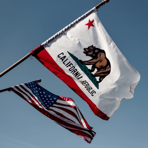 california and american flags waving in the wind against a blue sky