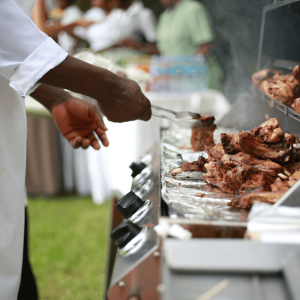 person in white smock cooking on a bbq grill