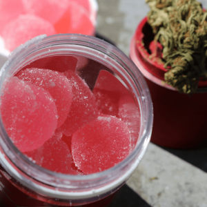 pink cannabis gummies pictured next to a grinder with flower on top