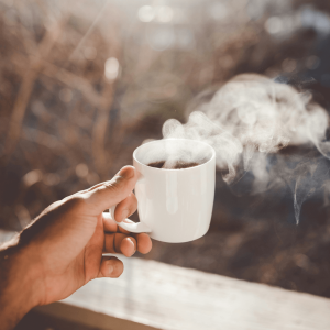 person holding a white ceramic mug of tea with steam