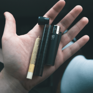 a hand holding a joint, vaporizer, and lighter