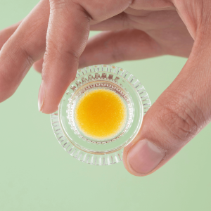 a hand holding light yellow cannabis concentrate in a jar