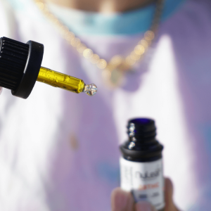 person in white t-shirt holding up cannabis dropper